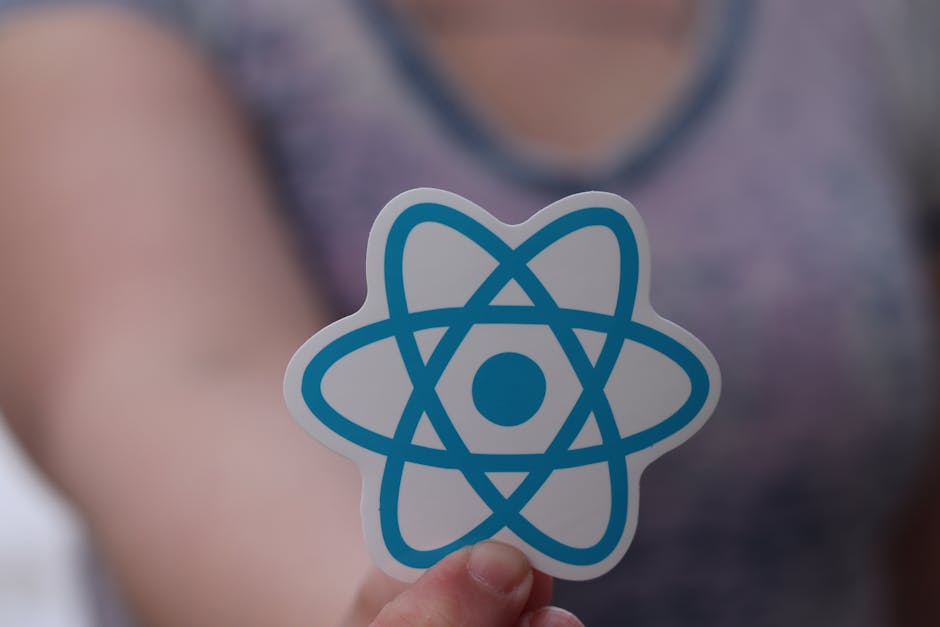 A person holding a paper cutout featuring a blue stylized atom symbol illuminated by soft, natural lighting. The individual is wearing a sleeveless purple top, with blurred background showcasing a cle